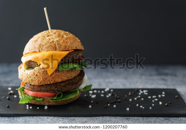 Vegetarian burger made of eggfruit hamburger, with
cheese, onion, tomato and cheese and integral bun. On textured
black board. 