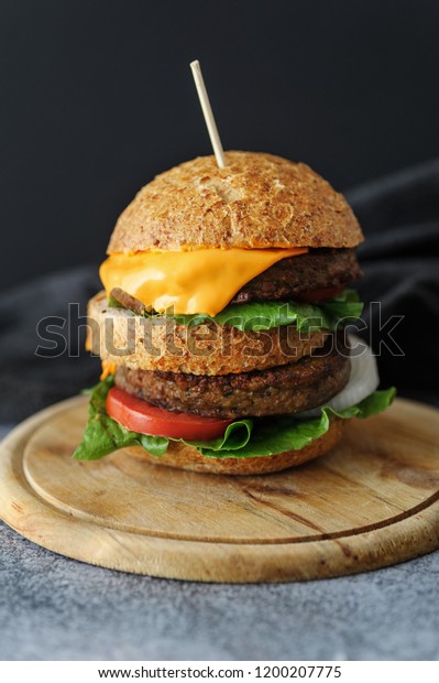 Vegetarian burger made of eggfruit hamburger, with\
cheese, onion, tomato and cheese and integral bun. On textured wood\
board. 