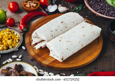 Vegetarian Burrito On Wooden Board Over Black Table Surrounded By Ingredients