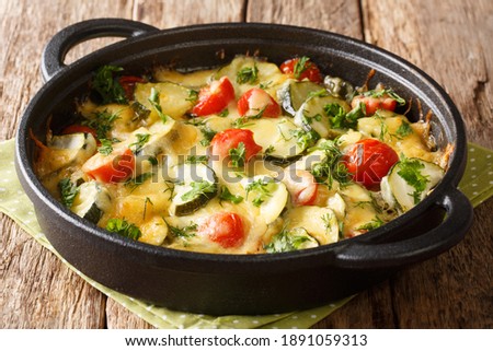 Vegetarian casserole with zucchini cheese and cherry tomatoes close-up in a pan on the table. 

