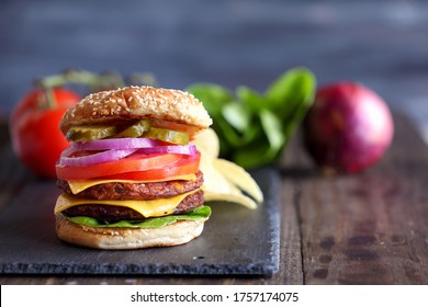 Vegetarian cheeseburger made with two meat substitute patties, slices of melted cheese, onions, pickles, lettuce, & tomato on a fresh sesame seed bun over a rustic dark background.  Blurred Background - Powered by Shutterstock