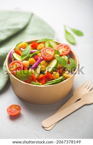 Vegetarian chickpea beans salad prepared with tomatoes, cucumber, red onion, cress salad and arugula in a paper bowl. Zero waste dishware such as wooden fork and paper bowl