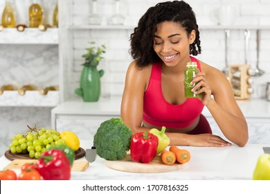 Vegetarian Food Concept. Portrait of smiling black girl drinking smoothie made of super foods, looking at vegetables on table