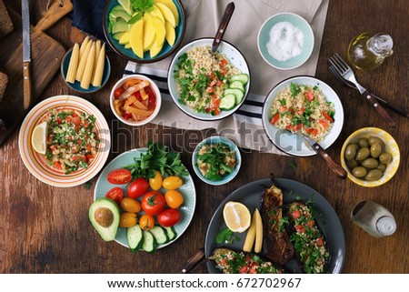 Vegetarian food concept. Set of healthy vegetarian food, salad with bulgur porridge and vegetables, stuffed eggplant, vegetables, mango, avocado and snacks on a wooden table, top view