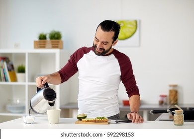 Vegetarian Food, Healthy Eating, People And Diet Concept - Man With Kettle Making Tea And Having Vegetable Sandwiches For Breakfast At Home Kitchen