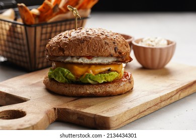 Vegetarian hamburger with cheddar cheese in whole grain bun and homemade oven baked sweet potato fries in a black deep frying basket net grid, wooden board, with ketchup sauce and mayonnaise - Powered by Shutterstock