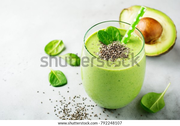 Vegetarian healthy green smoothie from avocado,\
spinach leaves, apple and chia seeds on gray concrete background.\
Selective focus. Space for\
text.