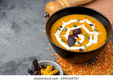 Vegetarian lentil soup puree garnished with pumpkin seeds and cream in a bowl on a black background. Horizontal, free space. Dish for Halloween.
