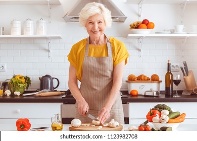 Vegetarian Older Woman Cooking Veggie Dinner, Toothy Smiling. Indoor, Studio Shoot, Kitchen Interior