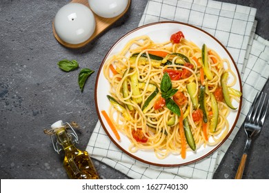 Vegetarian pasta. Pasta spaghetti with zucchini, carrot and tomatoes on grey stone background. Top view with copy space.