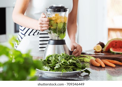 Vegetarian preparing vegan smoothie with rucola, citrus, cucumber in kitchen with carrots on countertop