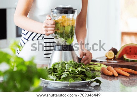 Vegetarian preparing vegan smoothie with rucola, citrus, cucumber in kitchen with carrots on countertop