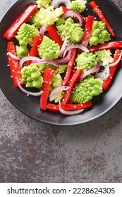 Vegetarian salad of steamed romanesco broccoli, bell pepper and red onion close-up in a plate on the table. Vertical top view from above
