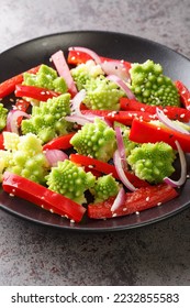 Vegetarian salad of steamed romanesco broccoli, bell pepper and red onion close-up in a plate on the table. Vertical
