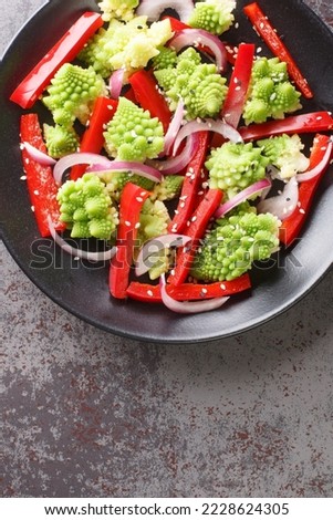 Vegetarian salad of steamed romanesco broccoli, bell pepper and red onion close-up in a plate on the table. Vertical top view from above