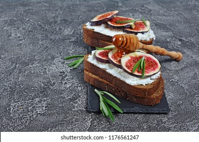 Vegetarian sandwich with figs, soft cheese, honey and rosemary on black slate board and gray concrete background with copy space - Powered by Shutterstock