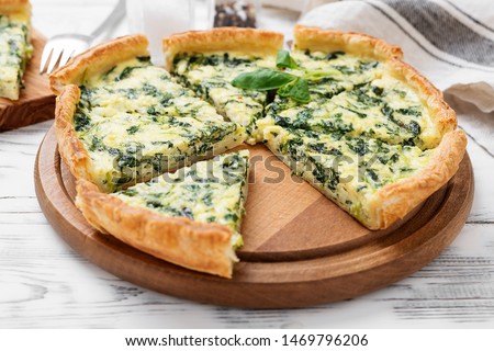 Vegetarian spinach pie or tart with feta cheese on white wooden background.