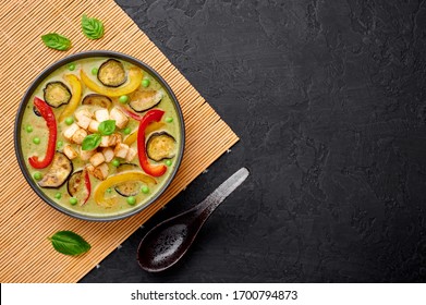 Vegetarian Thai Green Curry with tofu in black bowl at dark slate background. Veg Green Thai Curry is thailand cuisine dish with green chillies paste, basil, spices and vegetables. Copy space