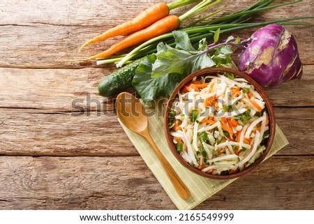 Vegetarian vegetable salad of kohlrabi, carrots, cucumbers and green onions seasoned with oil close-up in a plate on a wooden table. Horizontal top view from above
