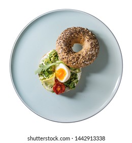 Vegetarian whole grain bagel sandwich with chopped avocado, cream cheese, sun dried tomatoes, egg, served on ceramic plate. Isolate on white background. Flat lay, space. Square image - Powered by Shutterstock