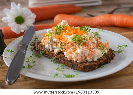 Vegetarian Wholemeal sandwich with cottage cheese and rasped carrots topped with cress and served on a white plate with knife on table background