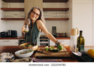 Vegetarian woman smiling at the camera while holding some green juice. Mature woman serving herself healthy plant-based food in her kitchen. Happy senior woman eating clean at home. - Powered by Shutterstock