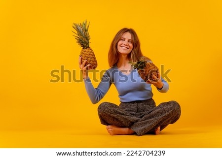 Vegetarian woman smiling with a cut pineapple sitting down, healthy living and tropical fruit concept