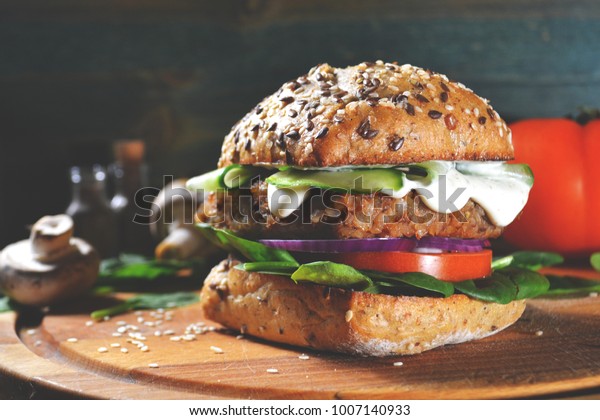 veggie, vegan burger with buckwheat, tomato,\
onion, vegan mayonnaise and spinach on a fresh bun with flax seeds\
and sesame, surrounded by spinach leaves, mushrooms, tomato, black\
pepper and spices.