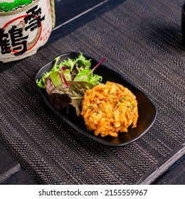 Veggie vegan tempura with salad in the traditional Japanese ramen restaurant, with a black plate on a black mat and Japanese fonts sake barrel translation: Snow Crane