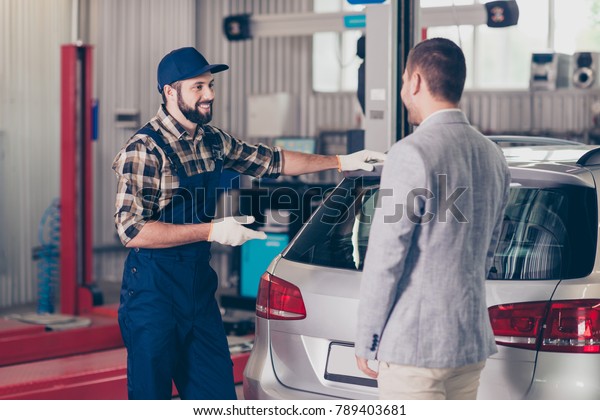 Vehicle breakdown, check, inspection, engineering\
concept. Cheerful specialist in blue overall, cap, checkered shirt\
enjoying conversation with client in formal outfit in work\
shop