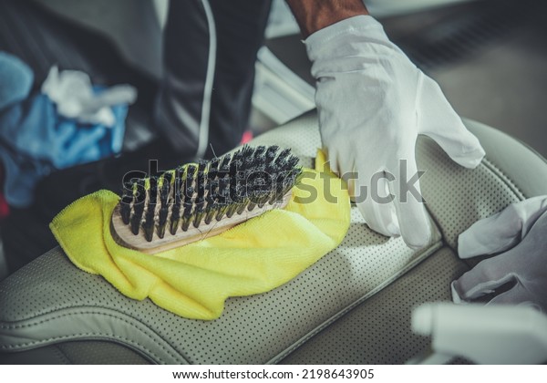 Vehicle Cleaner in White\
Gloves Precisely Cleaning Car Leather Seats Using Cloth and Brush\
to Maintain Its Good Looking Interior. Professional Auto Detailing\
Services Theme.