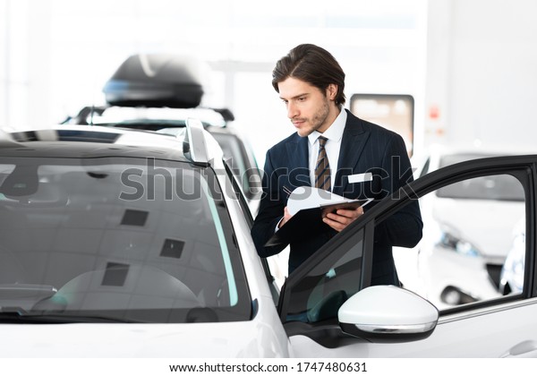 Vehicle\
Dealership. Car salesperson with clipboard checking auto\
specifications in local dealership\
showroom