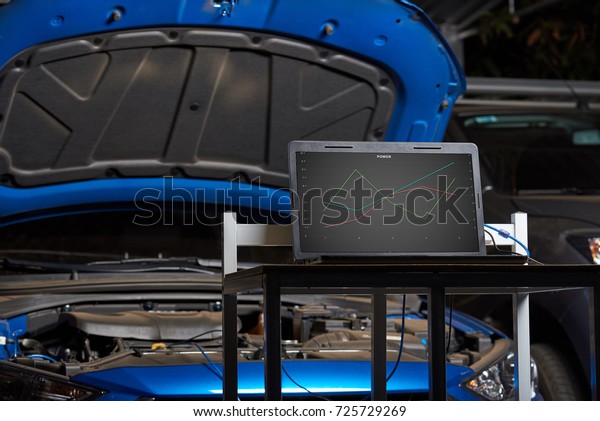 Vehicle diagnostic table station with\
statistic on laptop open car hood\
background