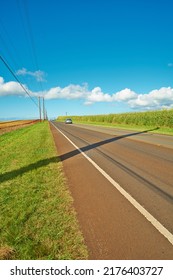 A Vehicle In The Distance Riding On An Open Highway Road Leading Through Agricultural Farms. Landscape Of Growing Pineapple Plantation Field With Blue Sky, Clouds, And Copy Space In Oahu, Hawaii, USA