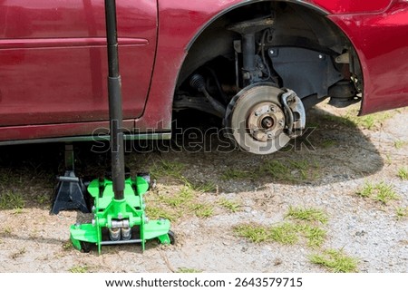 Vehicle is elevated on jack, exposing brake assembly wheel hub in grassy outdoor area.