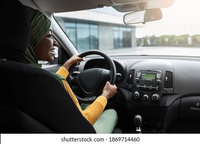 Vehicle Insurance Concept. Happy Black Muslim Lady In Hijab Sitting On Driver's Seat In Car Keeping Steering Wheel, Religious Lady Making Test Drive In Her New Vehicle, Over Shoulder View, Copy Space