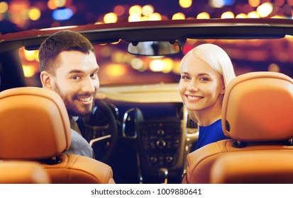 Vehicle, Luxury And People Concept - Happy Couple Driving In Convertible Car Over Night City Lights Background