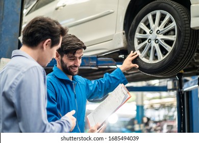 Vehicle Maintenance Handsome Man Servicer Explain Car Condition, Point At Vehicle Part To Asian Customer In Garage. Automotive Mechanic Hold Automotive Checklist Document. Car Repair Service Concept.