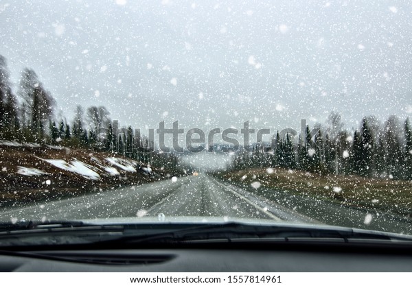 Vehicle safety, winter. Car driving in dangerous winter\
weather with poor visibility during snowfall and mist on the\
highway, concept for safety in traffic, copy space. Blurred view in\
car windshield 