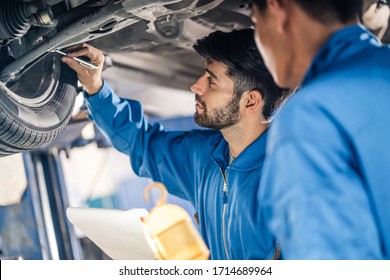 Vehicle Service Maintenance Handsome Mens Checking Under Car Condition In Garage. Automotive Mechanic Pointing Flash Light On Wheel Following Maintenance Checklist Document. Car Repair Service Concept