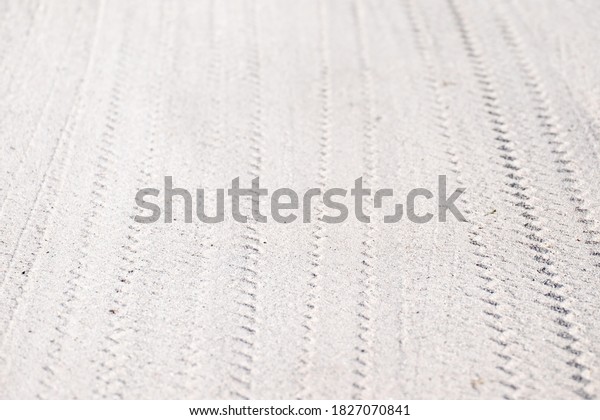 Vehicle tire patterns\
in white sand. The wheels have made a triangle pattern and multiple\
lines. There\'s a slight curve to the pattern. The sand is a fine\
white gritty. 