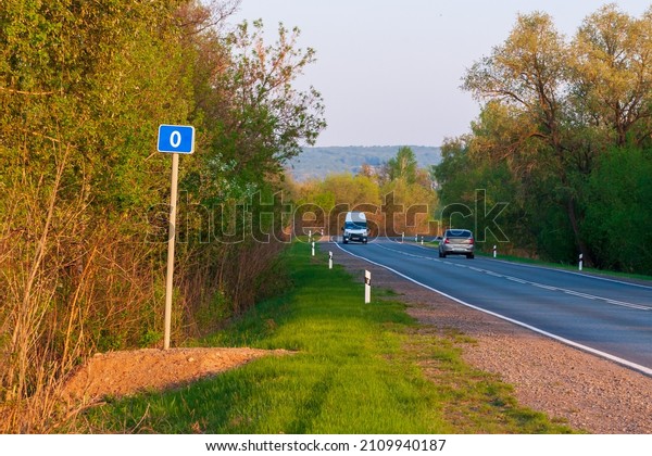 Vehicles passing by\
Kilometer marker 0 (zero) mark indicating the start of the route.\
Road sign zero\
kilometer.