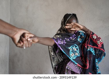 Veiled black African girl with her hand covering her eyes, pulled by the hand of an adult towards an atrocious fate; girl child abuse concept