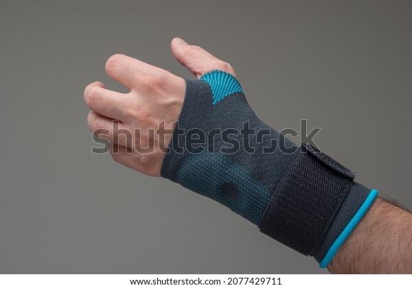 Velcro wrist stabilizer cast\
worn by Caucasian male hand. A blue split brace meant to aid Carpel\
Tunnel syndrome. Close up studio shot, isolated on gray\
background.