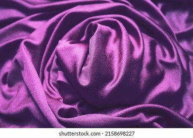 Velour fabric, similar to silk. Textiles in a folds, beautiful waves, twisted into a circle. Purple, pink, magenta shades on the drapery. Sewing material for dresses, furniture upholstery, curtains