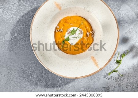 Velvety carrot cream soup with coconut cream swirl, top view on a speckled ceramic plate.