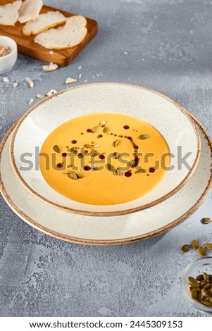 Velvety Pumpkin Soup Garnished with Pepitas and Olive Oil on a Rustic Ceramic Plate.