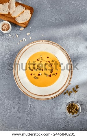 Velvety pumpkin soup topped with pumpkin seeds and a swirl of cream, served in a two-toned bowl, top view.
