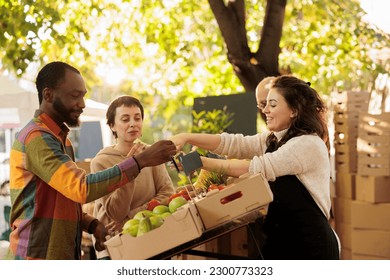 Vendor offering samples to customers while selling home-grown fruits and vegetables at local farmers market. Young multiracial family couple tasting natural organic produce while visiting food fair