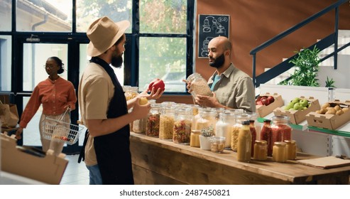 Vendor offers buyer bulk products, presenting middle eastern shopper selection of pasta, herbs and sauces. Young man buying organic produce at nearby eco friendly supermarket. Handheld shot. - Powered by Shutterstock